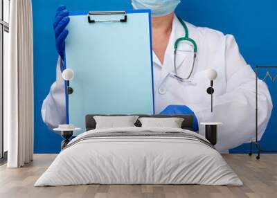 female doctor dressed in a white medical gown and blue latex gloves holds a folder with an empty blue sheet of paper Wall mural