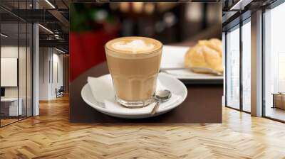 flat white coffee in a transparent glass with white foam, behind eclair cake Wall mural