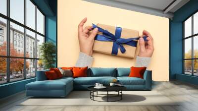 two female hands hold a gift paper box on a beige background Wall mural