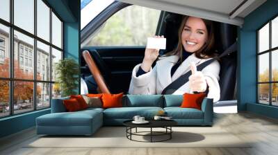 Beautiful young girl sitting in white car showing an empty white card and thumbs up hand sign Wall mural