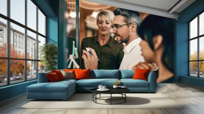 Putting their heads together to perfect the plan. Shot of a group of businesspeople having a brainstorming session on a glass wall in a modern office. Wall mural