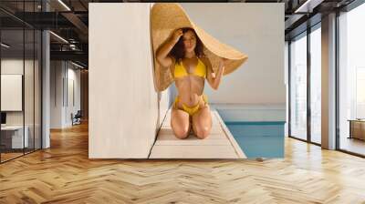 Attractive woman hiding from hot sun under big straw hat Wall mural