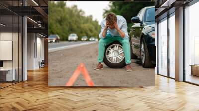 Car breakdown, tired man sitting on spare tyre Wall mural