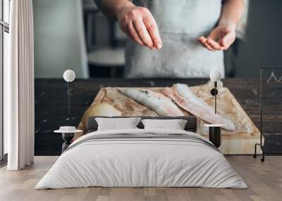 Chef hands salting raw fish over cutting board Wall mural