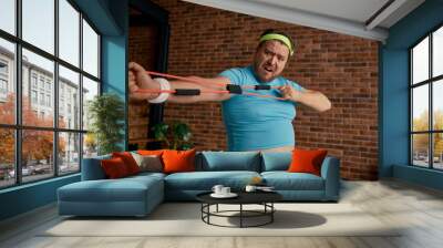 Comic chubby man in sportswear fooling around with fitness equipment Wall mural