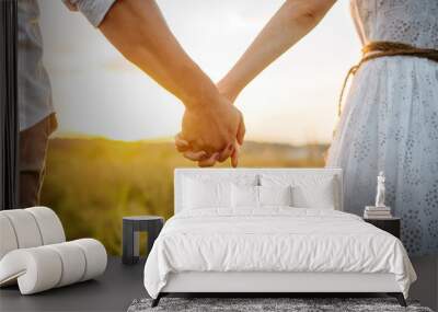 Couple hold hands in green field on sunset Wall mural