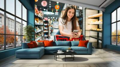 Female customer uses mobile phone in supermarket Wall mural