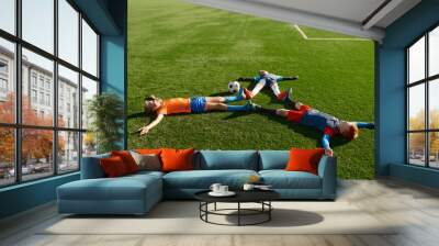 Happy tired football player lying like star on green field Wall mural