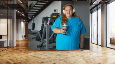 Portrait of young overweight woman wearing sportive clothes and headphones at gym Wall mural