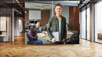 Smiling male IT specialist holds laptop in office Wall mural