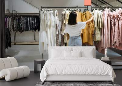 Woman choosing elegant dress in clothing store Wall mural