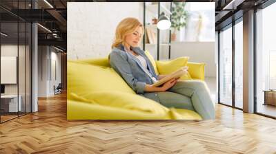 Young woman reading a book on cozy yellow couch Wall mural