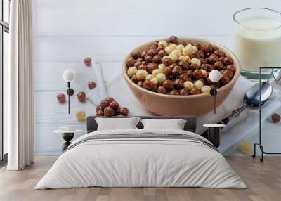 Bowl full of ready-to-eat healthy vegetarian cereals in shape of cocoa and vanilla balls served with spoon and glass of milk prepared for breakfast on white wooden background. ai generated Wall mural