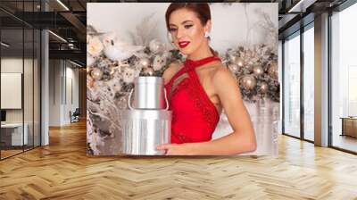  A girl in a red dress stands with many gifts in her hands, against the background of fireplace and christmas tree. Girl in a red dress with gifts in her hands on the background of a Christmas tree.Gi Wall mural