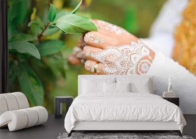 Closeup of bride hands with beautiful wedding mehendi touching green leaves Wall mural