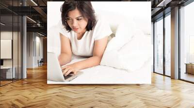 Smiling woman using a laptop while lying on her bed Wall mural