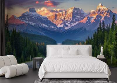 A long, straight road stretching towards towering snow-capped mountains, with the peaks glowing in the early morning light and the road lined by evergreen trees Wall mural