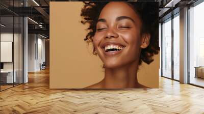 Beautiful natural woman with bare shoulders, laughing carefree, enjoying a beauty treatment, beige background Wall mural