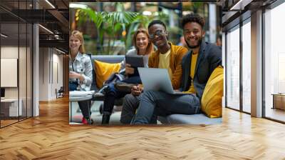 Multicultural businesspeople working in an office lobby. Group of happy businesspeople smiling while sitting together in a co-working space. Young entrepreneurs collaborating on a new project. Wall mural