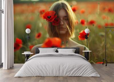 Mysterious young woman obscuring her face with bright red poppies in a field, creating a serene and whimsical summer outdoor portrait. Wall mural