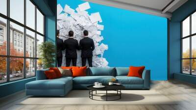 Three men in suits stand before a towering pile of paper, symbolizing overwhelming work or stress against a bright blue background. Wall mural