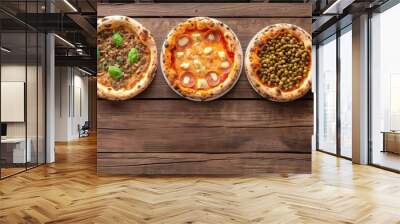 An array of pizzas featuring a wide range of toppings is displayed on a wooden surface, providing a feast for the eyes and a temptation for the taste buds. Wall mural