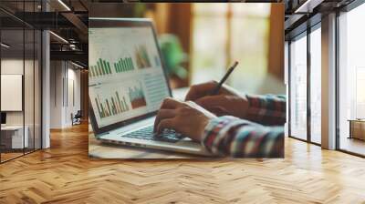 An individual examines complex financial charts displayed on a laptop screen Wall mural