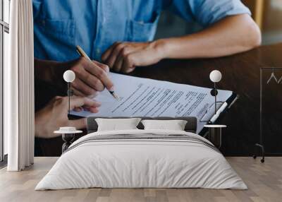 Close up of customer signing a paper document for buying house. Estate agent pointing finger showing where to sign on wooden desk. Agreement and Real estate concept. Wall mural