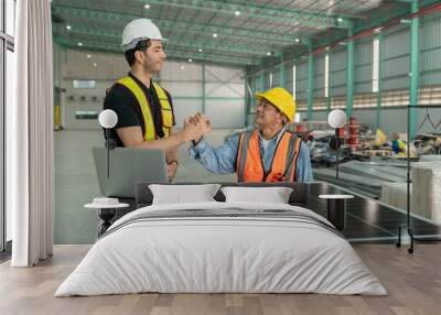 Two engineers in safety vests shaking hands after completing solar panel installation inside an industrial warehouse, symbolizing teamwork and project success. Wall mural