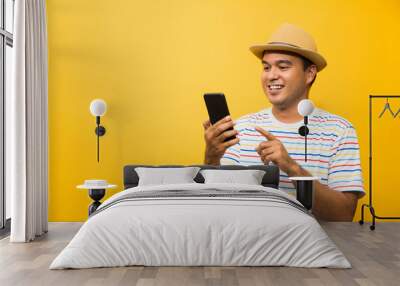 Asian man happy with his smartphone on yellow background. young man using looking at smartphone. Wall mural