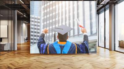 Happy graduate. Happy Asain man in graduation gowns holding diploma in hand on urban city background. Wall mural