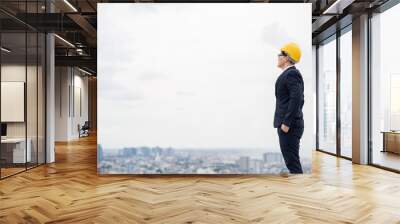 Young handsome asian civil engineer standing wearing helmet yellow hard hat in business suite on building urban cities background. Wall mural