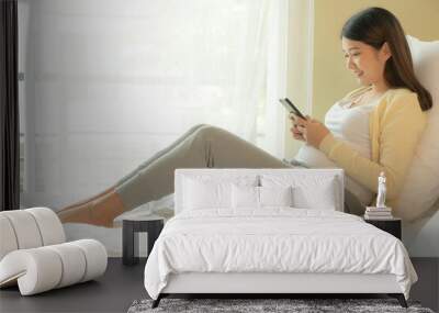 Young Asian pregnant woman using mobile phone in bedroom. Wall mural