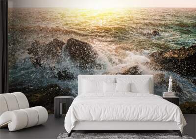 Water waves and splashes breaking on rocks in sunset of sea background Wall mural