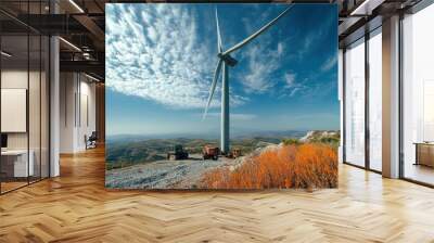 A large wind turbine stands tall against a blue sky with white clouds, surrounded by construction vehicles and a rugged landscape. Wall mural