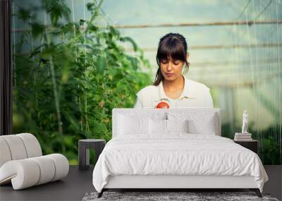 Female farmer working in greenhouse, checking plants and using tablet Wall mural