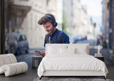 Portrait of handsome young man with cell phone and headphones listening to music on the street Wall mural