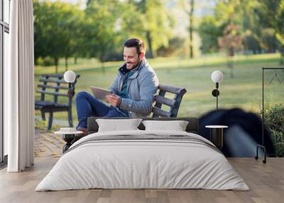 Positive Businessman at the park with tablet sitting on a bench Wall mural