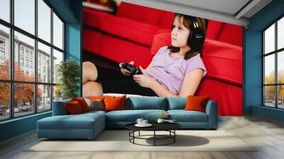 Teen girl wearing headphones and holding a video game controller. Concept of kids gaming at home. Daily technology in children life. Wall mural