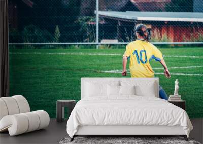 Young girl playing football at local stadium outside on green grass ready to kick the ball. Youth league, girls football team. Wall mural