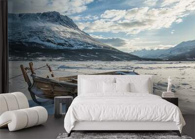 Old wooden boat lays on a frozen lake covered in snow with snow capped mountains in the background Wall mural