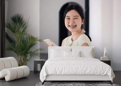 Happy young asian millennial woman smiling with braces in casual outfit and using smartphone, positive and confident female teenager Wall mural