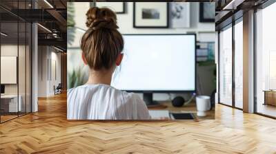 Over shoulder shot of a young woman using computer in front of an blank white computer screen in home. Wall mural