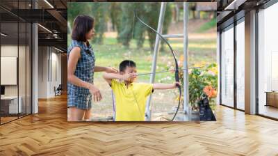 Asian boys are archery in camp adventure and the woman standing behind Background  blurry tree. Wall mural