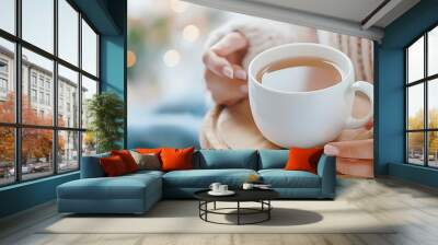 A cozy scene featuring a person holding a white coffee cup on a wooden tray, surrounded by soft textiles and warm lighting. Wall mural