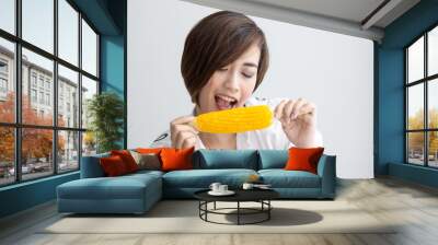 Asian girl eating yellow corn at home. Wall mural