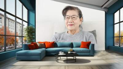 Happy Asian senior woman wearing eyeglasses and sitting on sofa at home, lifestyle concept. Wall mural