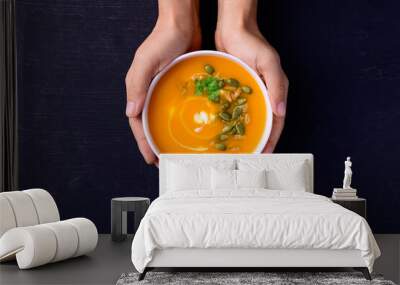 Butternut squash pumpkin soup in bowl holding by hand on black background, Homemade food in autumn season, Top view Wall mural