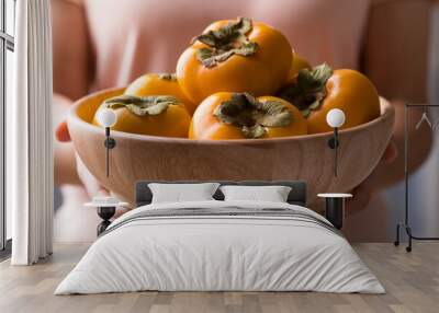 Ripe persimmon fruit in wooden bowl holding by womand hand Wall mural