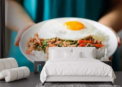 Thai food, stir-fried holy basil with minced pork and fried egg  (Pad Kaprao Moo Kai Dao) on plate holding by hand Wall mural